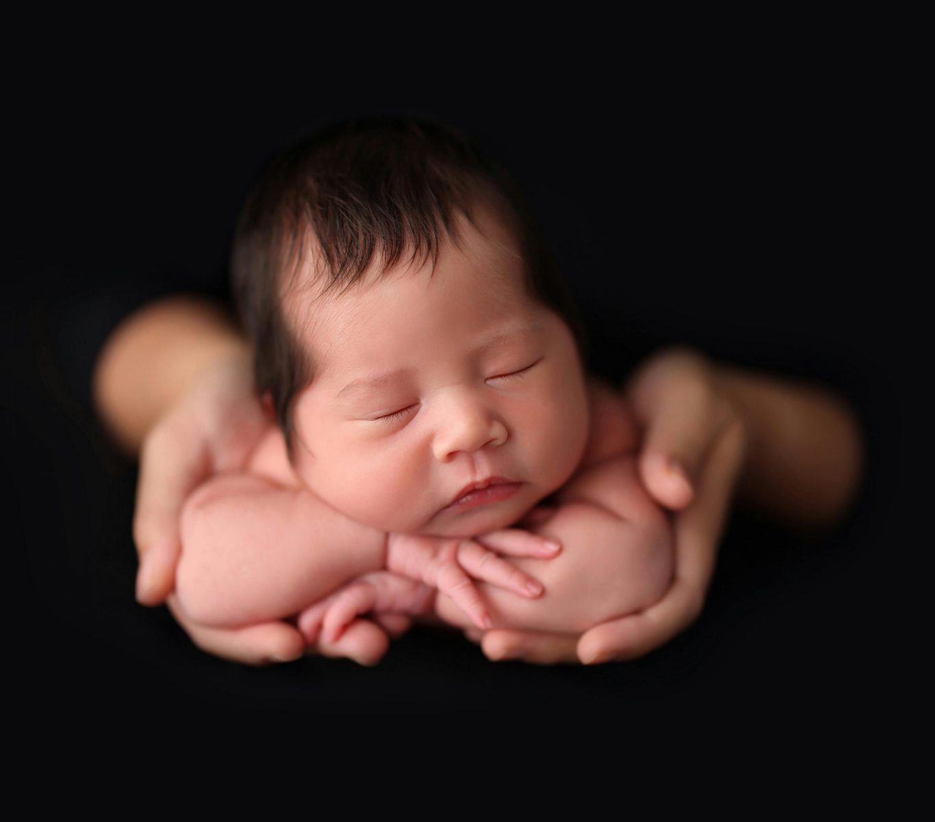 Close-up of an adorable Asian newborn baby sleeping peacefully cradled in loving hands.