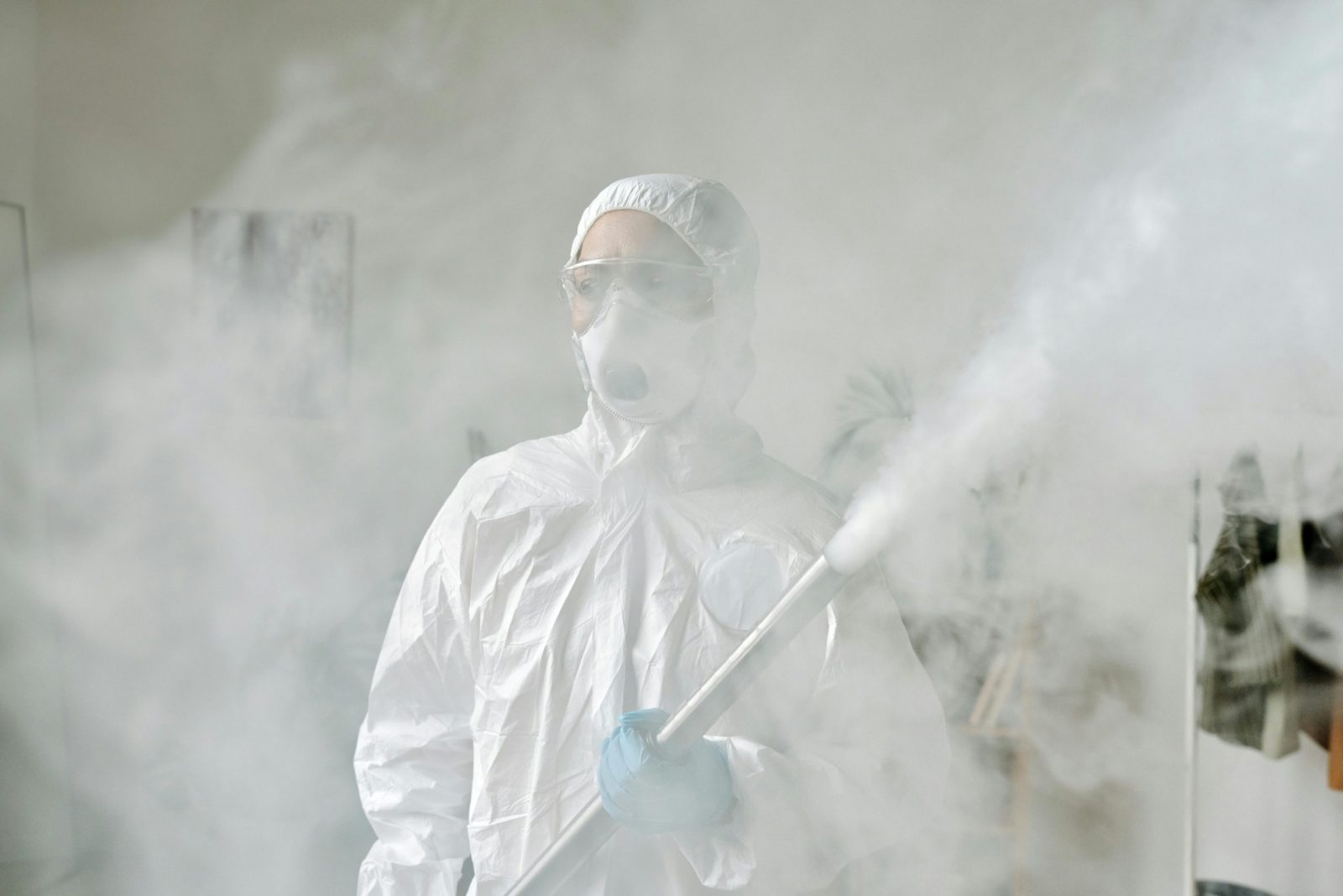 Person in protective gear fumigating an area indoors amid smoke for disinfection.
